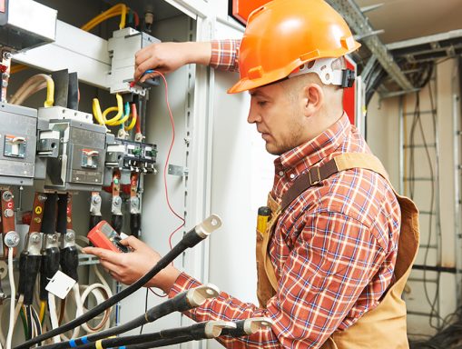 Electrician in a hard hat working on electrical panels with tools.