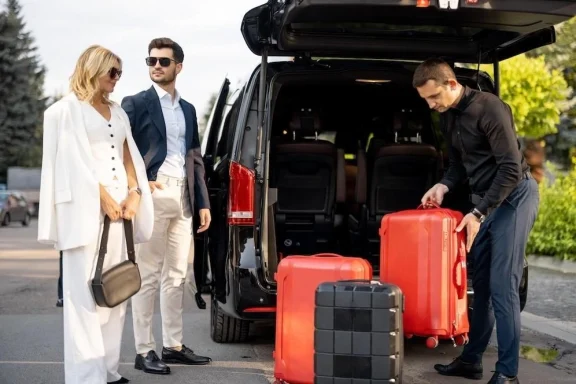 A group of travelers loading red suitcases into a parked vehicle.